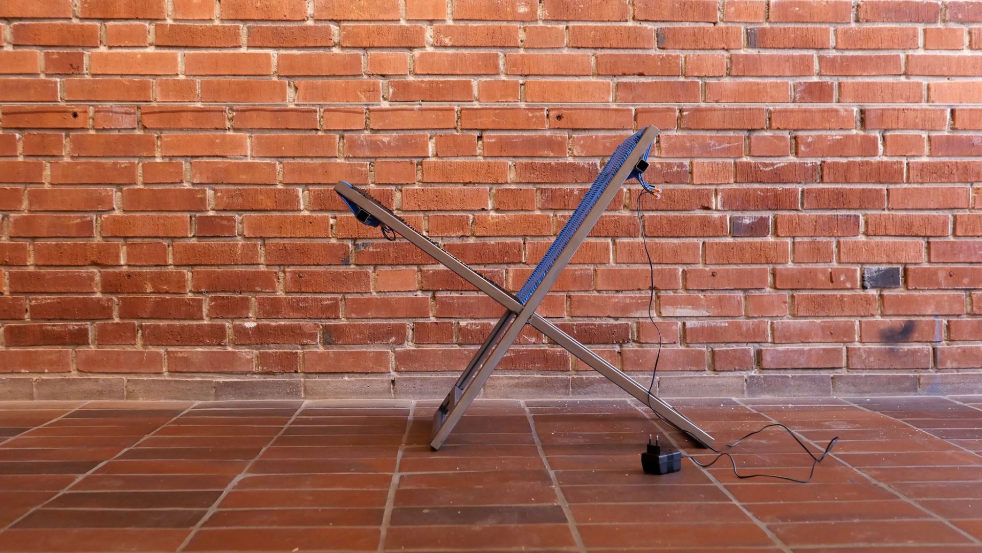 Stolen chair — woven blue seat on welded steel X-frame against brick wall